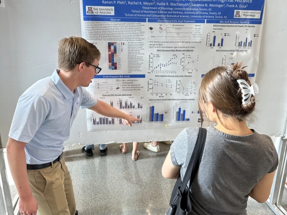 A person pointing at a poster explaining their research to another person.